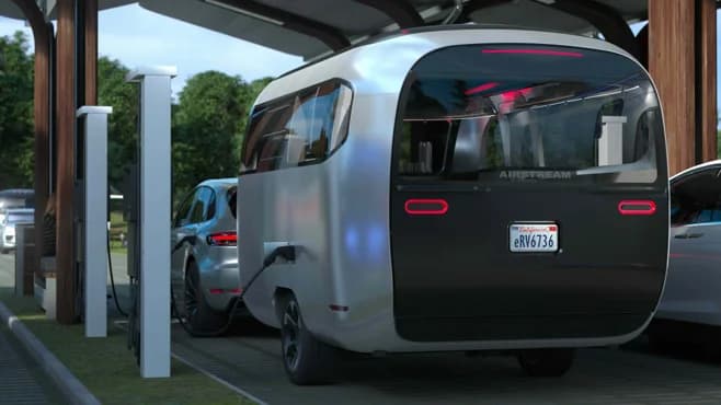 A futuristic Airstream trailer charging beside an electric vehicle